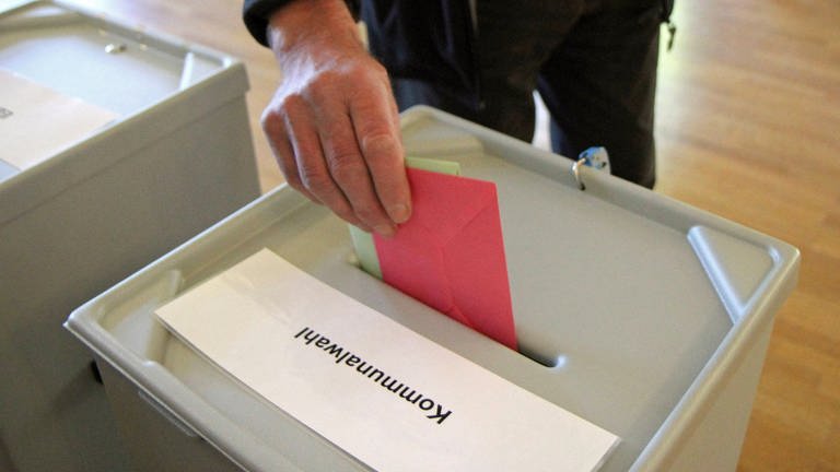 Eine Hand steckt Wahlumschläge in eine Wahlurne: Im kommenden Jahr stehen in Baden-Württemberg die Kommunalwahlen an. (Foto: IMAGO, IMAGO / Eibner)
