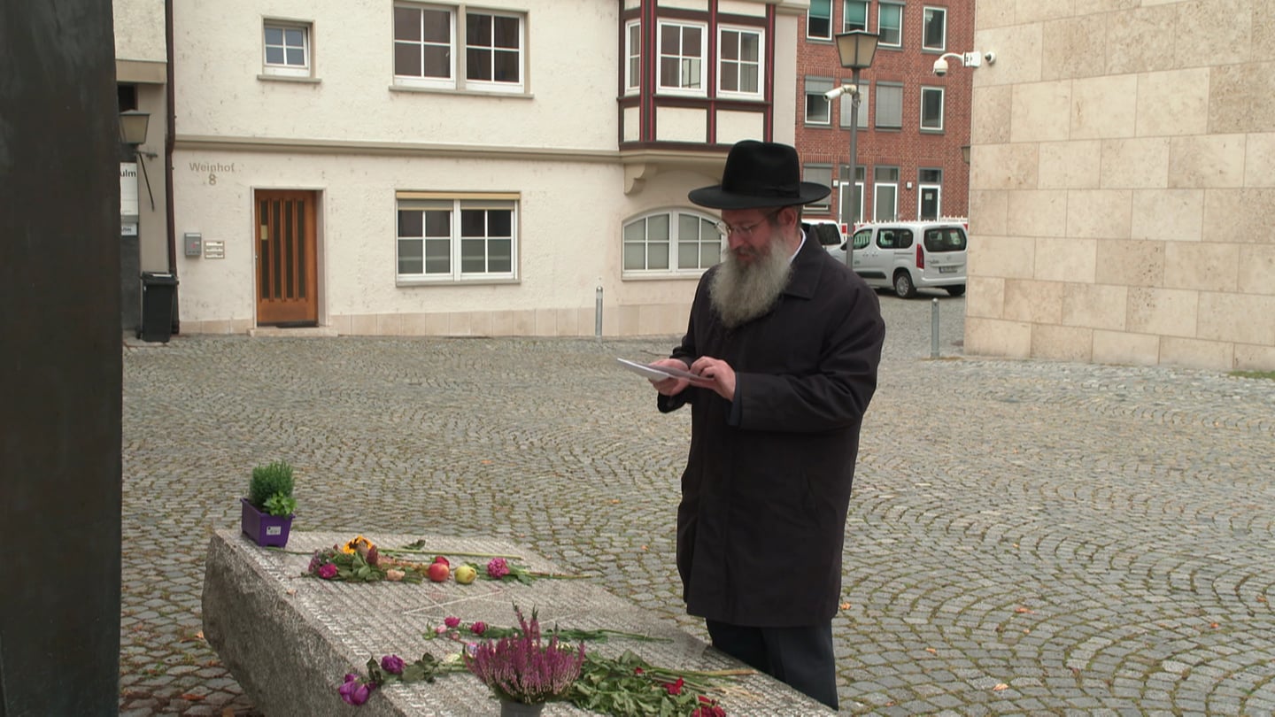 Ein Mann mit Bart und Hut betrachtet einen Stein mit Blumen. Zeichen der Solidarität mit Israel - der Ulmer Rabbiner Shneur Trebnik, Mitglied im Rat der Religionen, betrachtet vor der Synagoge die Blumen und Briefe der Menschen. (Foto: SWR)