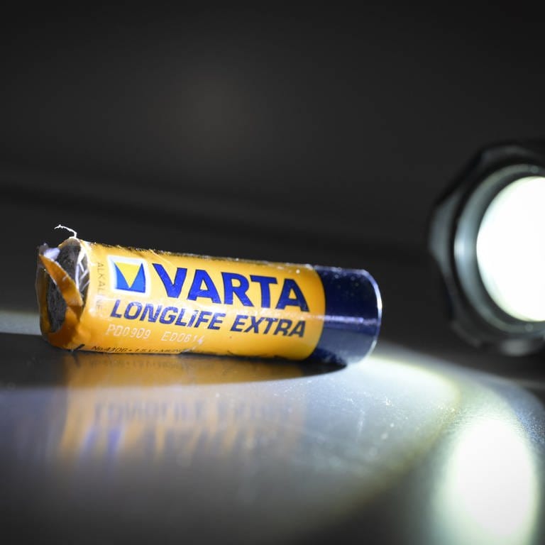 Eine verbeulte Batterie wird von einer Taschenlampe angestrahlt. Beim kriselnden Batteriehersteller VARTA aus Ellwangen läuft es weiterhin nicht rund.  (Foto: dpa Bildfunk, picture alliance/dpa | Felix Kästle)