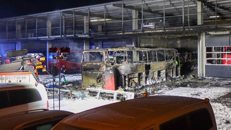 Ein komplett ausgebrannter Reisebus vor einer Halle. An der Seite stehen ein Feuerwehrauto und weitere geparkte Fahrzeuge. Bei dem Brand in Günzburg sind zwei Reisebusse komplett zerstört worden. (Foto: Mario Obeser)
