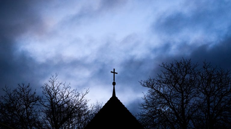 Dunkle Wolken ziehen über das Kreuz auf einer evangelischen Kirche in der Region Hannover hinweg.  (Foto: picture-alliance / Reportdienste, Picture Alliance)