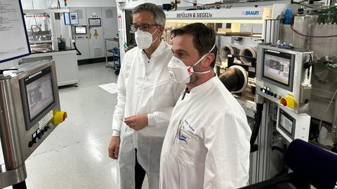 Markus Hölzle und Stefan Guther (vorne) vom ZSW schauen zu, wie die Maschine dünne Elektroden übereinanderstapelt. Ulmer Forschende entwickeln umweltfreundliche Natrium-Ionen-Batterie. (Foto: SWR, Justus Madaus)