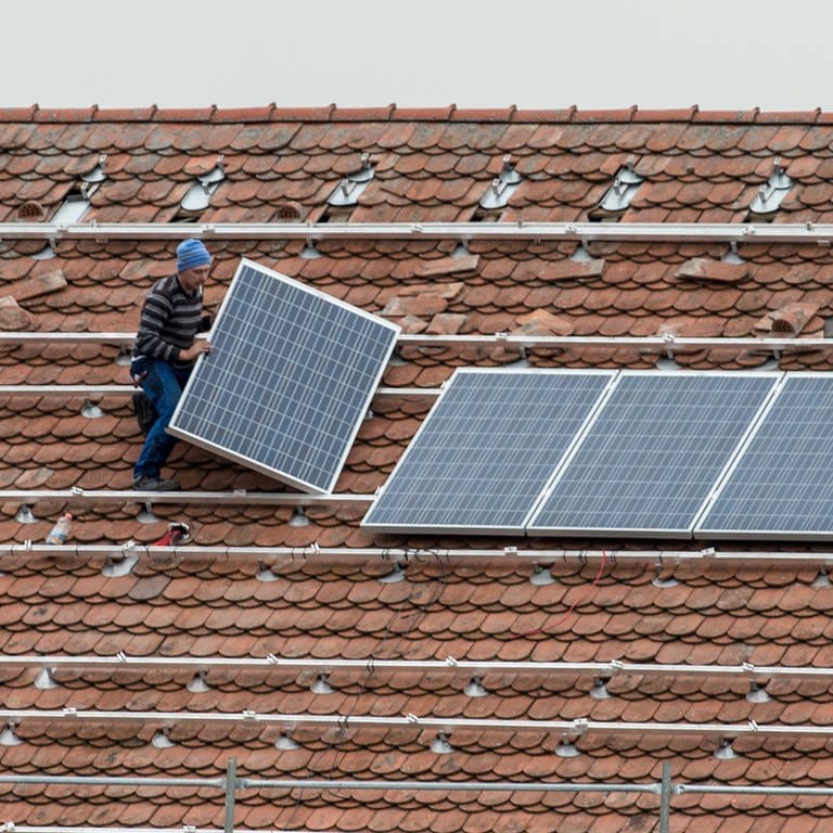 Mann bringt auf einem Dach Photovoltaikmodule an