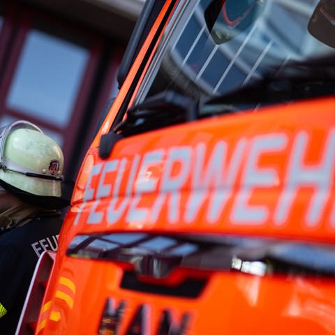 Die Front eines Feuerwehrautos mit dem Schriftzug "Feuerwehr", daneben ein Feuerwehrmann. Bei einem Brand in der Innenstadt von Munderkingen sind am Samstag zwei Menschen schwer verletzt worden.  (Foto: dpa Bildfunk, picture alliance/dpa | Marijan Murat)