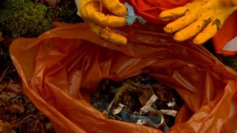 Ein Helfer zeigt einen Müllsack mit kleinen Teilen von Plastikverpackungen.
