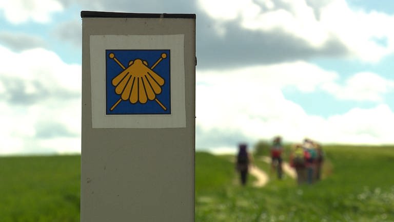 Eine gelbe Muschel auf blauem Grund hilft Pilgern auf dem Jakobsweg, den richtigen Weg zu finden.