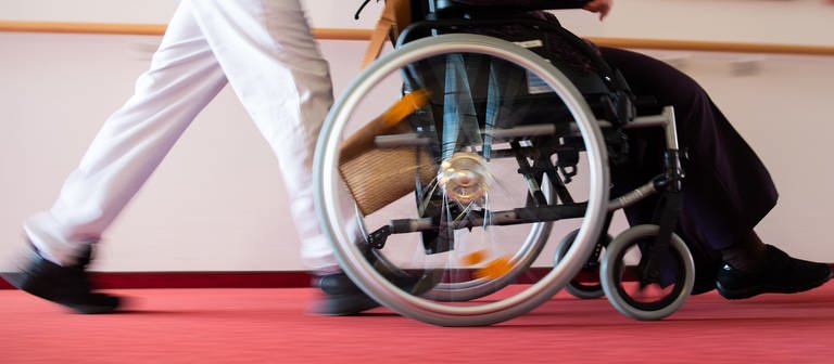 Eine Pflegekraft schiebt einen Rollstuhl mit einer Bewohnerin über den Flur eines Altenheims. (Foto: dpa Bildfunk, picture alliance/Tom Weller/dpa)