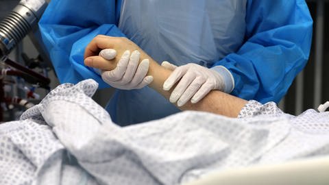 Eine Pflegerin hält die Hand eines Patienten auf einer Corona-Intensivstation (Foto: dpa Bildfunk, picture alliance/ dpa/ dpa-Zentralbild/ Bernd Wüstneck)