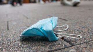 Eine blassblaue Corona-Maske liegt auf dem Boden einer Fußgängerzone. In Rheinland-Pfalz steigen die Coronazahlen. Die Einschränkungen für Ungeimpfte könnten deshalb zunehmen. Für die Maskenpflicht sind laut Landesregierung keine Änderungen geplant. (Foto: dpa Bildfunk, picture alliance/ dpa/ Daniel Bockwoldt)