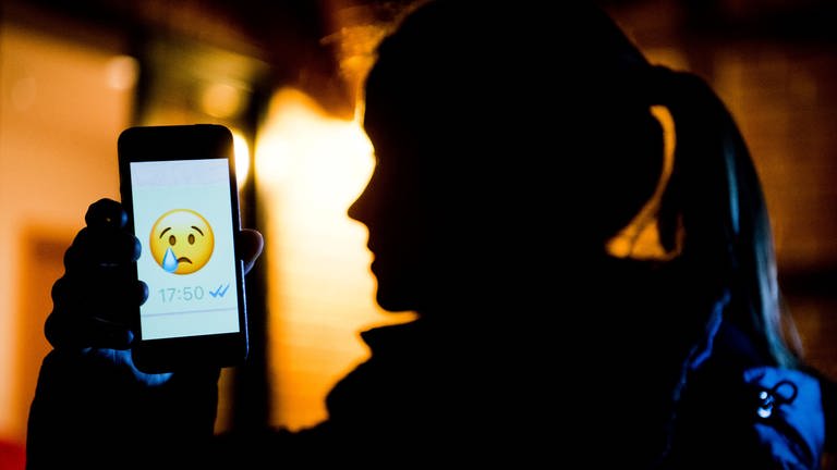Symbolbild: Ein junges Mädchen zeigt das Display eines Smartphones mit einem weinenden Emoji. (Foto: dpa Bildfunk, picture alliance/dpa | Julian Stratenschulte)