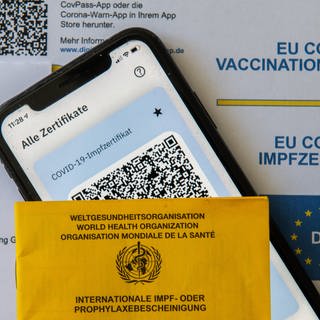Ein Impfpass und ein Smartphone, auf dem die App CovPass läuft, liegen auf einem Impfzertifikat, das von einer Apotheke ausgestellt wurde. (Foto: dpa Bildfunk, picture alliance/dpa | Stefan Puchner)