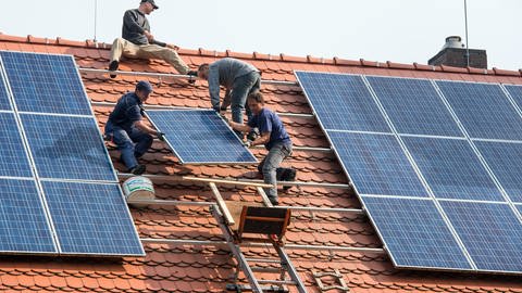 Installateure befestigen Solar-Panele für eine neue Photovoltaik-Anlage auf dem Dach eines Wohn-Hauses.