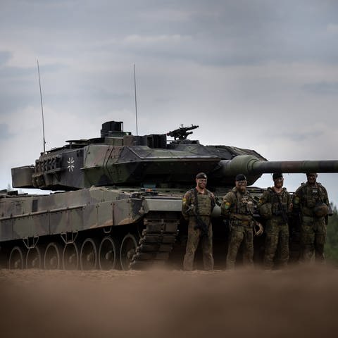 Soldaten stehen vor einem Leopard-2-Panzer der Bundeswehr, der von der NATO eingesetzt wird. (Foto: dpa Bildfunk, picture alliance/dpa | Michael Kappeler)