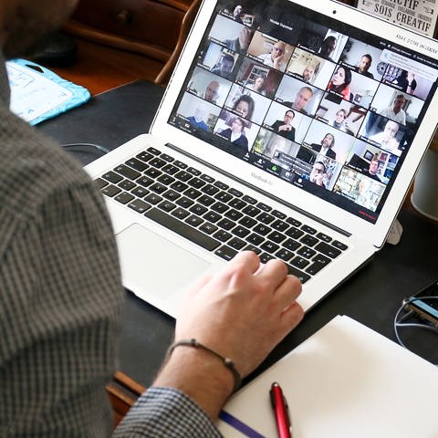 Ein Mann sitzt vor einem Bildschirm mit einer großen Videokonferenz (Foto: IMAGO, IMAGO / Hans Lucas)