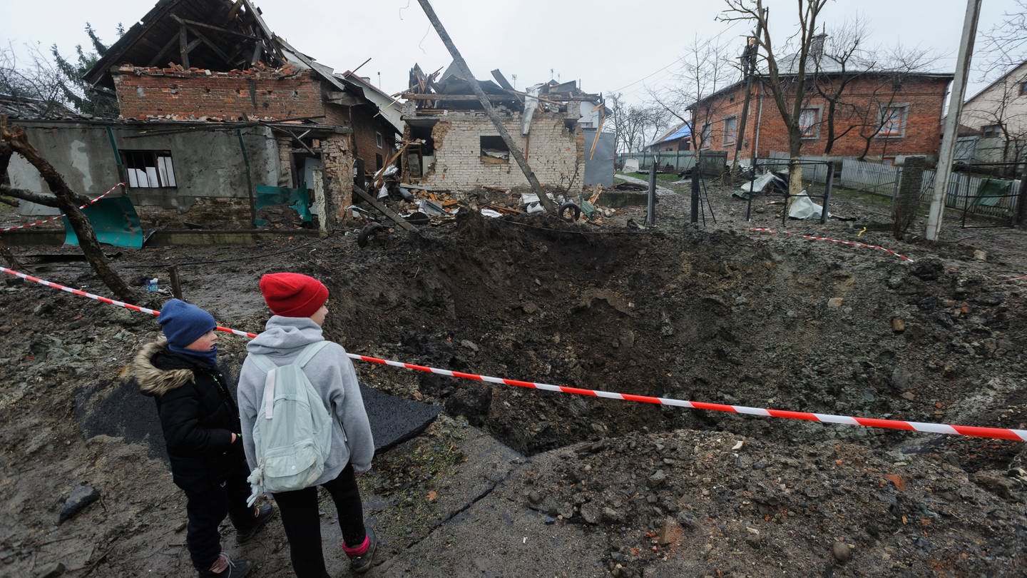 Zwei Kinder betrachten einen Krater, der nach ukrainischen Angaben durch eine Explosion in einem Wohngebiet nach russischem Beschuss entstanden ist. (Foto: dpa Bildfunk, picture alliance/dpa/AP | Mykola Tys)