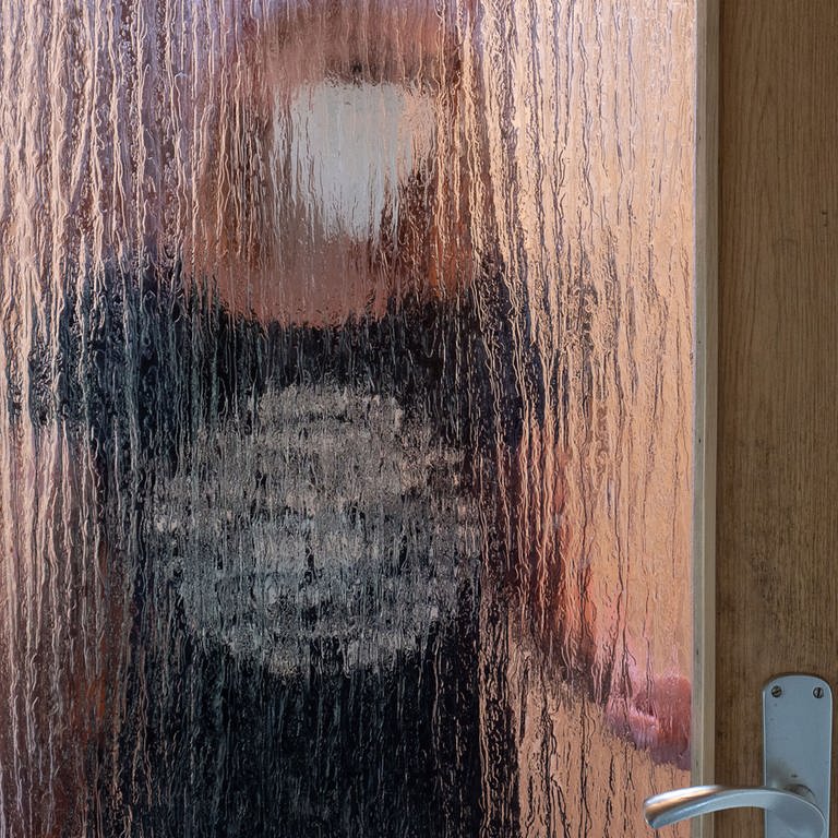 Eine Frau steht in Isolation von ihrer Familie hinter einer geschlossenen Glastür und trägt eine FFP2-Maske. (Foto: dpa Bildfunk, picture alliance/dpa | Sebastian Gollnow)