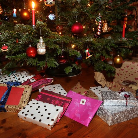 Verpackte Weihnachtsgeschenke liegen in einem Wohnzimmer unter einem geschmückten Weihnachtsbaum. (Foto: dpa Bildfunk, picture alliance/dpa | Karl-Josef Hildenbrand)