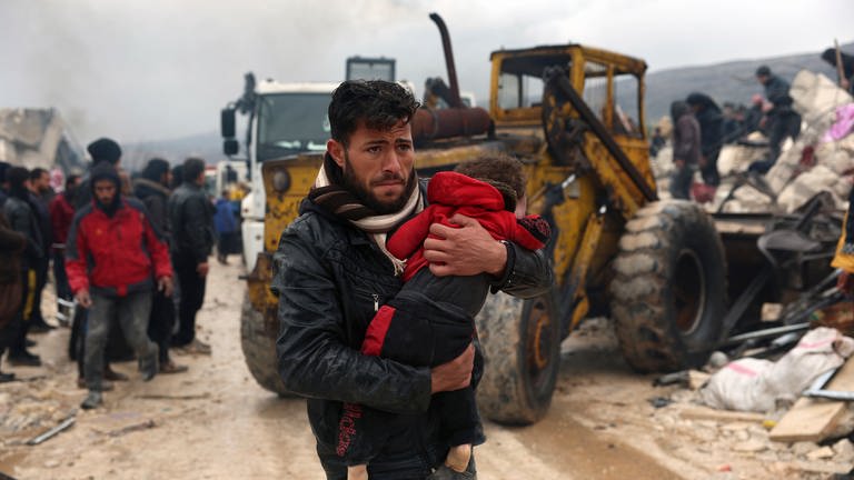 Ein Mann trägt ein Kleinkind durch Trümmer in einer türkischen Stadt. (Foto: dpa Bildfunk, picture alliance/dpa/AP | Ghaith Alsayed)