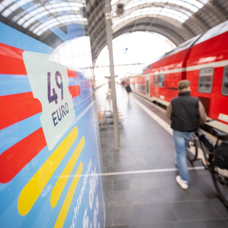 Ein Mann geht mit seinem Fahrrad an einer Deutschlandticket-Werbung und einem Regionalzug vorbei (Foto: dpa Bildfunk, picture alliance/dpa | Sebastian Gollnow)