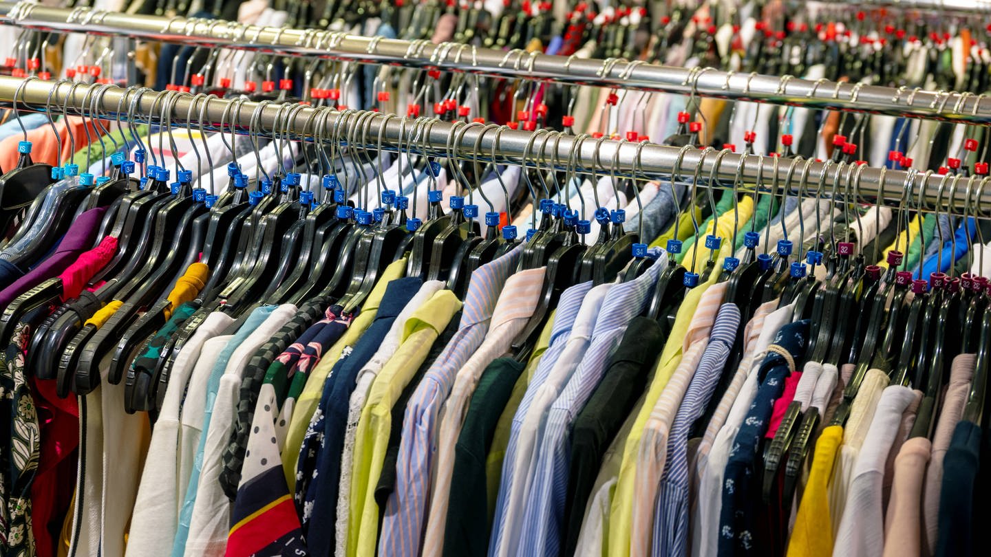 Textilien als Massenware: Verschiedenfarbige Hemden, Blusen und Westen werden im Einzelhandel als Massenware auf endlosen Kleiderstangen angeboten. (Foto: IMAGO, IMAGO / Zoonar)
