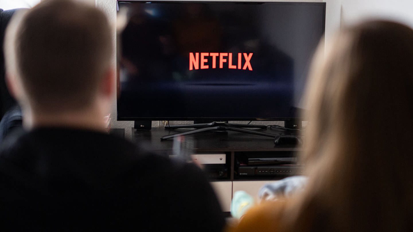 Ein Paar sitzt vor dem Fernseher, auf dem das Netflix-Logo zu sehen ist. (Foto: dpa Bildfunk, picture alliance/dpa | Daniel Reinhardt)