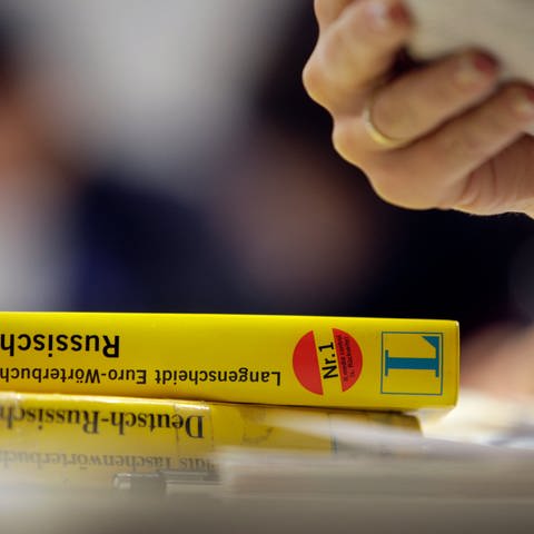 Auf einem Tisch bei einem Sprachkurs liegen zwei Wörterbücher für Russisch, während die Hand einer Frau ein Arbeitsblatt hält. (Foto: dpa Bildfunk, picture alliance / dpa | Rolf Vennenbernd)