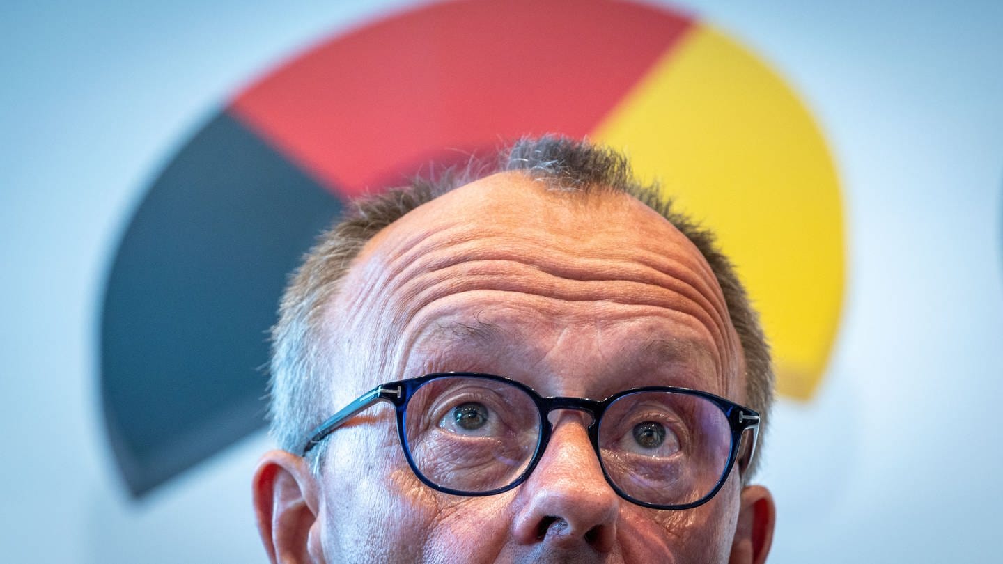 CDU-Chef Friedrich Merz hat bei einer Pressekonferenz die Stirn in Falten gelegt, während die deutschen Nationalfarben seinen Kopf umgeben. (Foto: dpa Bildfunk, picture alliance/dpa | Jens Büttner)