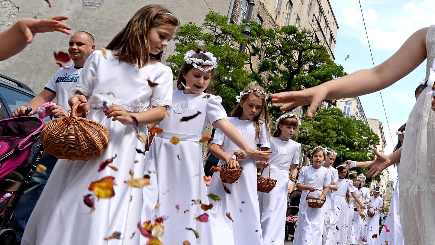 Erstkommunikantinnen in Weiß streuen Blütenblätter auf die Straße. (Foto: dpa Bildfunk, dpa picture alliance)