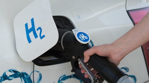 Der Tankdeckel Autos mit der Aufschrift "H2" für Wasserstoff steht offen und der Tank wird an einer Zapfsäule befüllt. (Foto: dpa Bildfunk, picture alliance / Sebastian Kahnert / dpa-Zentralbild / dpa)