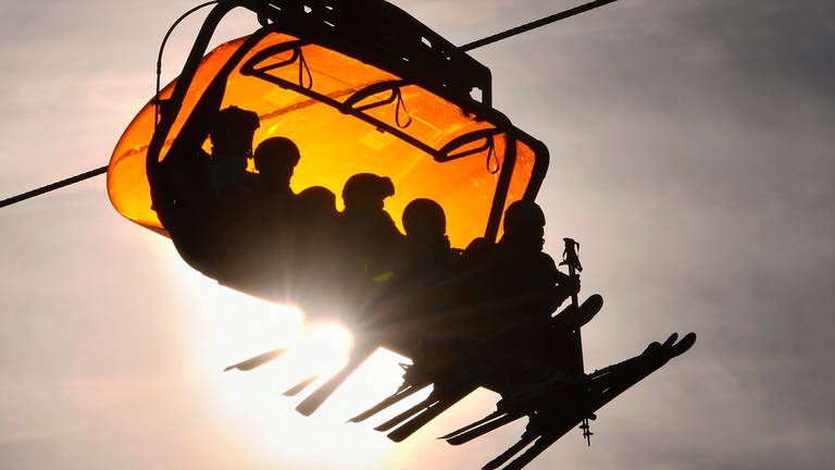 Skifahrer benutzen einen großen Sessellift in einem Skigebiet, während die Sonne tief steht.