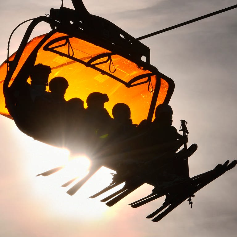 Skifahrer benutzen einen großen Sessellift in einem Skigebiet, während die Sonne tief steht. (Foto: dpa Bildfunk, picture alliance/dpa/TASR | Milan Kapusta)