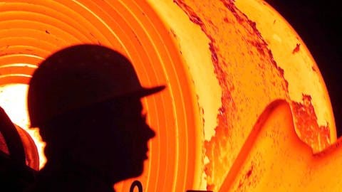 Ein Stahlarbeiter im ThyssenKrupp-Werk in Bochum steht vor einem glühenden sogenannten Stahlcoil, das etwa 1200 Grad heiß ist, und in der sogenannten Coilbox auf- und abgewickelt wird. (Foto: dpa Bildfunk, picture-alliance/ dpa | Rolf Vennenbernd)