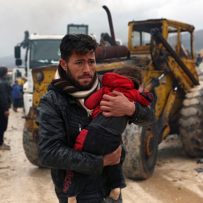 Ein Mann trägt ein Kleinkind durch Trümmer in einer türkischen Stadt.