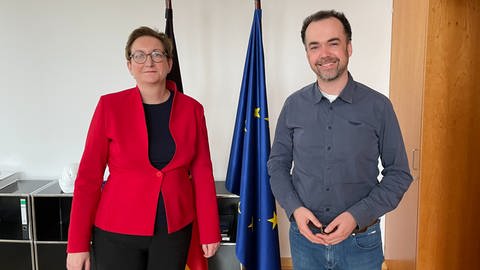 SWR-Korrespondent Oliver Neuroth steht neben Bundesministerin Klara Geywitz im Ministerium für Wohnen, Stadtentwicklung und Bauwesen, vor einer Europa-Fahne.  (Foto: SWR)