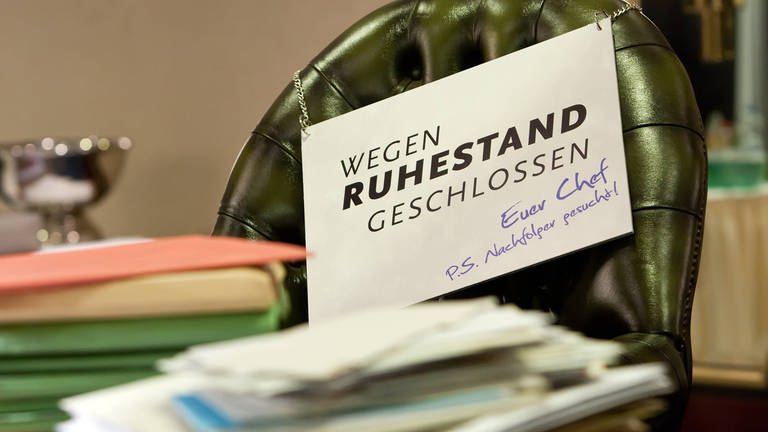 Symbolbild mit vollem Schreibtisch und Schild "Wegen Ruhestand geschlossen" (Foto: IMAGO, IMAGO / Marius Schwarz)