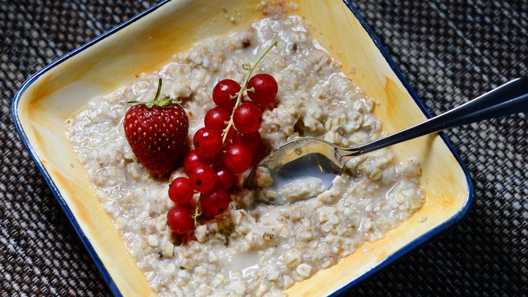 Eine Schale mit Porridge und Obst steht auf einem Frühstückstisch.
