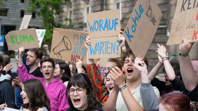 Mit selbstgebastelten Pappschildern, darunter eines mit der Aufschrift "Worauf warten?", demonstrieren Teilnehmer einer Kundgebung von Fridays for Future (FFF).