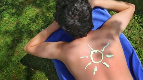 Ein junger Mann hat mit Sonnencreme eine Sonne auf den Rücken gemalt.