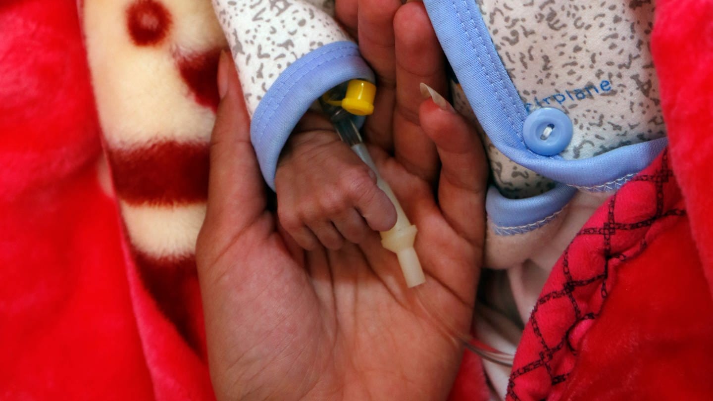 Eine kleine, dünne Kinderhand liegt in der Hand einer Erwachsenen. (Foto: dpa Bildfunk, picture alliance/dpa/XinHua | Mohammed Mohammed)