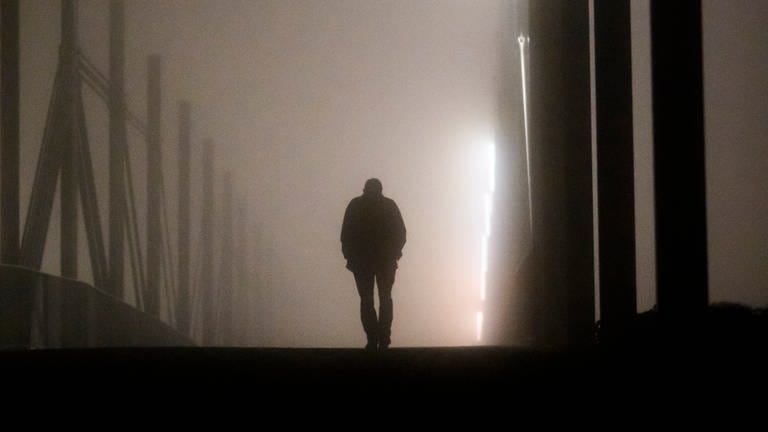Ein Mann geht am frühen Morgen bei Nebel alleine über eine Brücke. (Foto: dpa Bildfunk, picture alliance/dpa | Julian Stratenschulte)