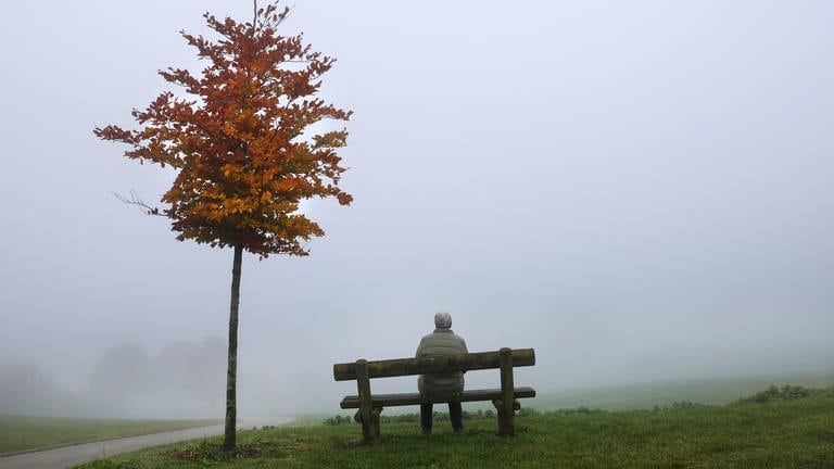 Ein älterer Mensch sitzt auf einer Bank im Nebel. Blickrichtung von hinten. (Foto: dpa Bildfunk, picture alliance/dpa | Thomas Warnack)