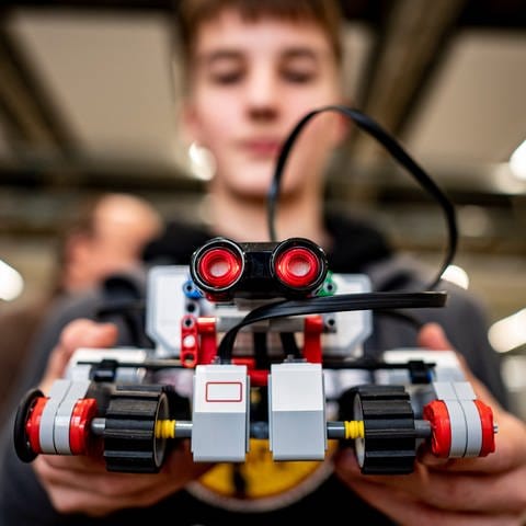 Ein Teilnehmer hält seinen selbst konstruierten Roboter in die Kamera, das Gerät ist etwa so groß wie ein Paar Schuhe (Foto: dpa Bildfunk, picture alliance/dpa | Fabian Sommer)