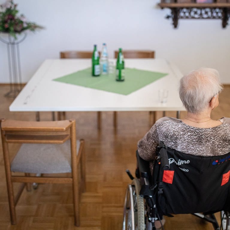 Ein ältere Frau im Rollstuhl sitzt in einem Pflegeheim an einem Tisch. Der Pflegeschutzbund Biva hat vor den Folgen einer sozialen Isolation von Pflegeheim-Bewohnern während des Corona-Lockdowns gewarnt (Archivbild).