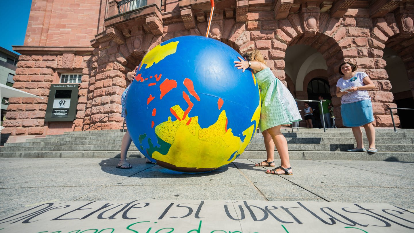 Teilnehmer der Aktion zum Erdüberlastungstag in Mainz stellen eine riesige Weltkugel auf dem Gutenbergplatz auf. Mit der Aktion will der 