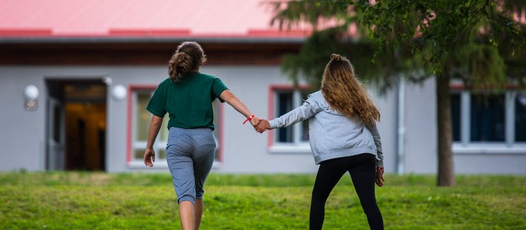 Zwei Schülerinnen gehen Hand in Hand auf dem Gelände eines Schullandheims spazieren.  (Foto: dpa Bildfunk, picture alliance/dpa | Andreas Arnold)