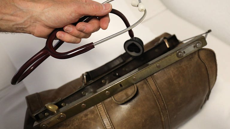 Hand hält Stethoskop vor einer Tasche (Foto: dpa Bildfunk, picture alliance/dpa | Oliver Berg)