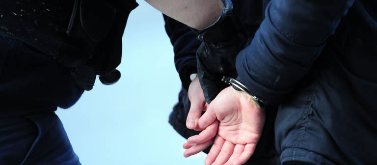 Ein Polizist führt einen mit Handschellen gefesselten Mann ab. (Foto: dpa Bildfunk, Picture Alliance)