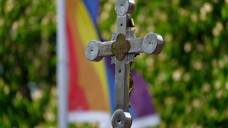 Ein Kreuz steht vor einer Regenbogen-Fahne.  (Foto: dpa Bildfunk, Picture Alliance)