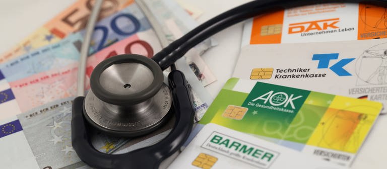 Geld, Krankenkassenkarten und ein Stethoskop  (Foto: dpa Bildfunk, dpa / Daniel Karmann)