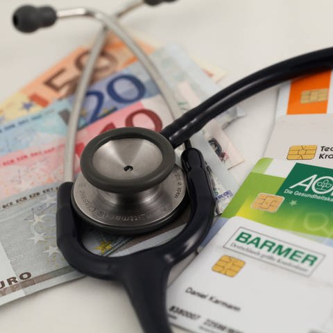 Geld, Krankenkassenkarten und ein Stethoskop  (Foto: dpa Bildfunk, dpa / Daniel Karmann)
